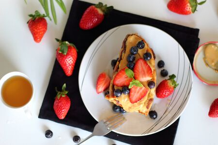 Delicious french toasts with berries, agave syrup and peanut butter in plate for breakfast on white table, top view, copy space.の写真素材