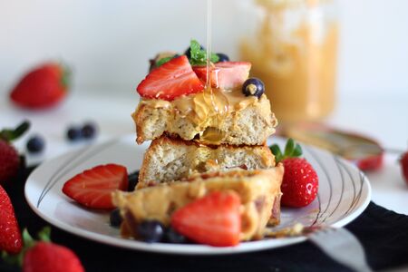 Pouring syrup over french toasts with peanut butter, strawberries and blueberries for breakfast.の写真素材