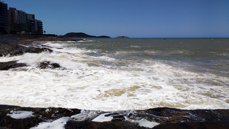 Rocks and rough sea foaming with buildings in the backgroundの写真素材