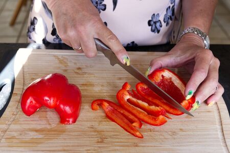 Frontal view close up shot of caucasian woman that is slicing red pepper in her kitchen.の写真素材