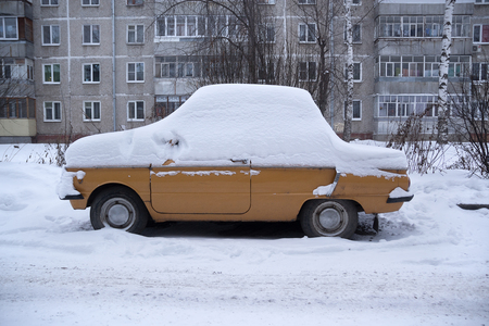 A car  covered with snow, standing in the middle of a winter streetの写真素材