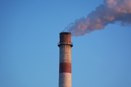 Chimney of a factory with white smoke and clear blue skyの写真素材