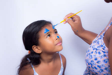 Mother painting daughter's face with blue paint and brush.の写真素材