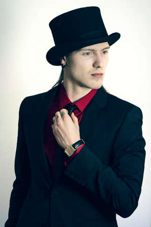 Handsome young guy in a top hat and suit with a gold watch on a white background.の写真素材
