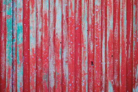 Old metallic shutter with red and blue turquoise peeling paint layers, grunge background or textureの写真素材