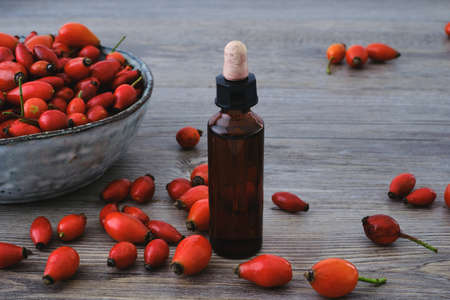 Dog rose (Rosa Canina) red rosehip oil extract on a glass dropper and natural red fruits on a bowlの写真素材
