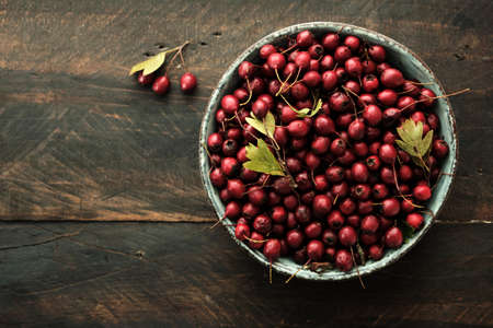 A bowl with hawthorn (Crataegus monogyna) red berries on dark rustic wooden table backgroundの写真素材
