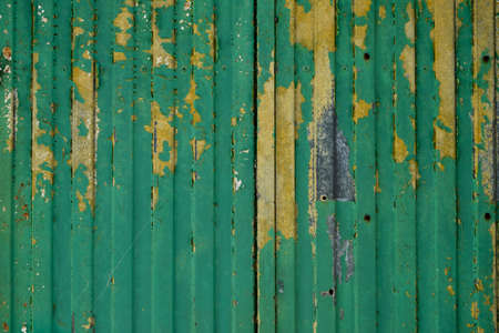 Old metal shutter with scraps of green and yellow paint, grunge backgroundの写真素材