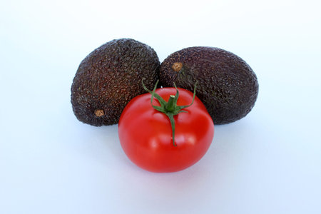 A tomato accompanied by fresh avocado on a white background