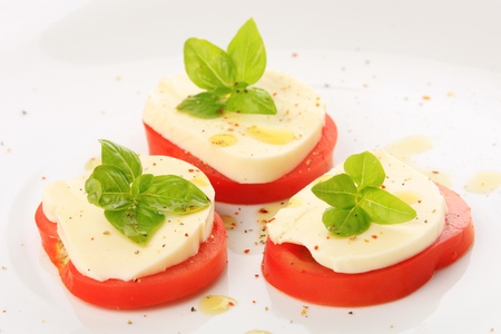 Served tomato with mozzarella and basil on white plateの写真素材