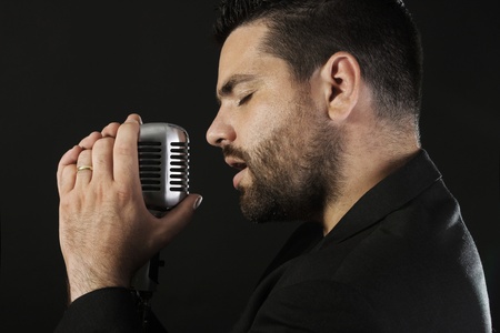 Portrait of male  singer  with old fashioned microphone against black background の写真素材