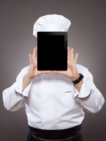 Chef behind the digital tablet against grey backgroundの写真素材