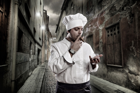 Chef with cognac and cigar smoking in dark streetの写真素材