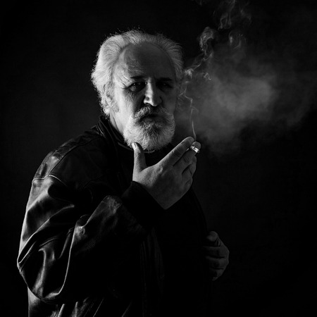 Grumpy man smoking against black backgroundの写真素材