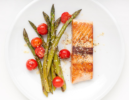 Salmon fillet with asparagus and cherry tomatoes on white plateの写真素材