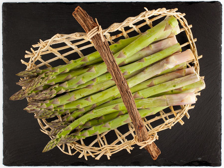 Green asparagus in wicker basket on black plateの写真素材