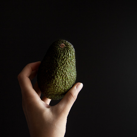 Small avocado in female hand against black backgroundの写真素材