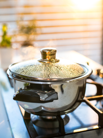 Boiling water in the pot on the stove in the eveningの写真素材
