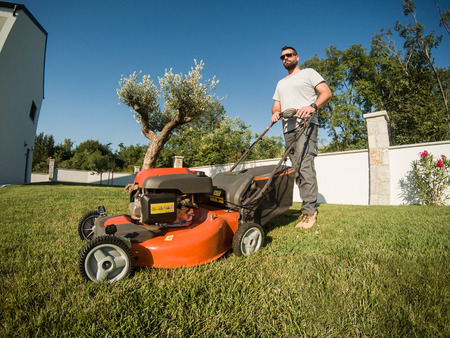 Wide angle of adult bearded male with lawnmowerの写真素材