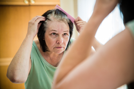 Senior woman checking her gray hair in the mirrorの写真素材