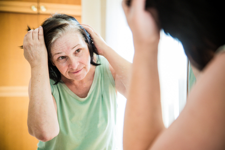 Senior woman checking her gray hair in the mirrorの写真素材