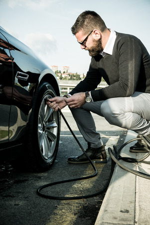 Bearded man checking tire pressure on his carの写真素材