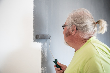 Funny senior man with beard painting the wallの写真素材