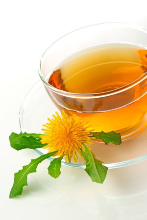 Dandelion tea in a transparent cup with dandelion flower and leaves on white backgroundの写真素材