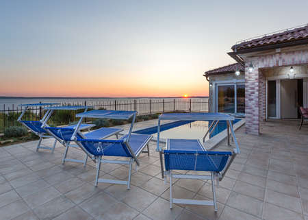 Stone villa with swimming pool and deck chairs at sunsetの写真素材