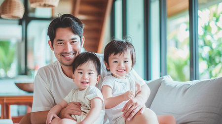 An oriental father with his two small children on the sofa at homeの素材