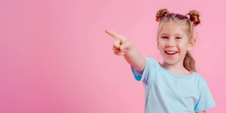 Smiling little girl pointing with finger on plain pink backgroundの素材