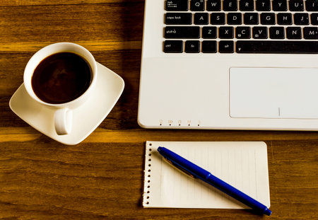 Office table with notepad, computer, pen and coffee cupの写真素材
