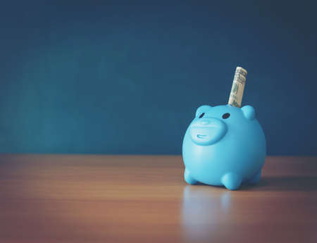 A piggy bank put on the stacking gold coins and blackboard house and clock on the vintage blue background, saving money for buy a new real estate or loan for planned investment in the future concept.の写真素材