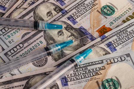 Close up view of a syringe with hypodermic needle and hundred dollar bill. Opiate and heroin overdoses have skyrocketed in recent years Iの写真素材