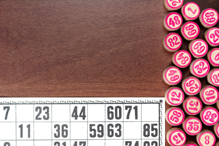 Board game lotto or bingo. Wooden lotto barrels with numbers and card on brown desk with copy space. Vintage game.の写真素材