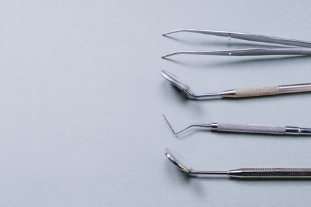 Dentist tools: two mirrors, dental probe and tweezers on gray background on right side.の写真素材