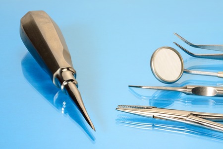 Dentist basic tools and root elevator on blue glass table: dental mirror, kornzange, explorer, forceps. Dental therapy and healthcare concept.の写真素材