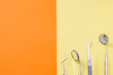 Dentist tools: two mirrors, explorer and tweezers on orange yellow bacrground, with copy space.の写真素材