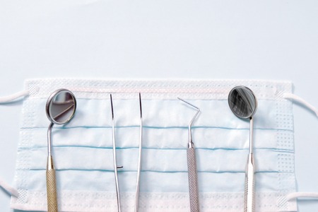Dentist base instruments: two mirrors, dental probe and tweezers lying on medical mask. On light gray background.の写真素材