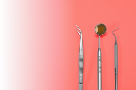 Dentist tools: mirror, dental probe and tweezers lying on living coral gradient background.の写真素材