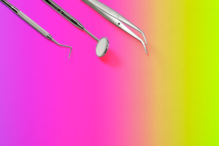 Dentist tools: mirror, dental probe and tweezers lying on purple green background.