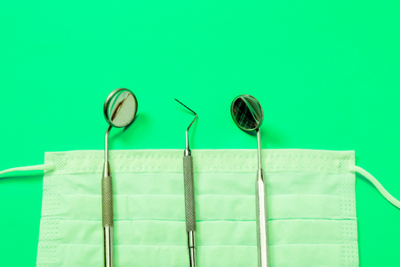 Dentist tools: mirror, dental explorer and tweezers lying on medical mask on neon green background.の写真素材