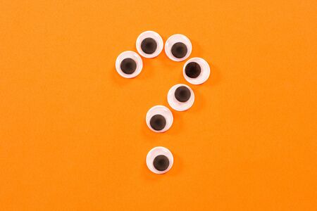 Googly eyes. Some crazy toy eyes on orange background. In the shape of question markの写真素材