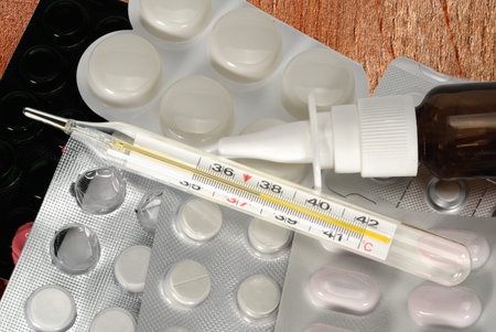 Classic mercury thermometer, nasal spray and pills blisters on wooden table. Cold and flu cure...