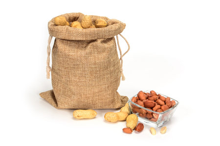Peanuts. Jute burlap sack full of peanuts and glass bowl with some peeled kernels. Isolated on white...