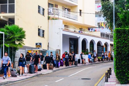 LLORET DE MAR, SPAIN - JULY 27, 2019: A group of rested and tanned tourists leaves the hotel and goes down the street with luggage. The concept of rest. Summer travel.のeditorial素材