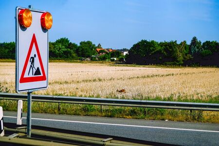 Road works on the highway and a small roe deer on freshly mown fieldの写真素材