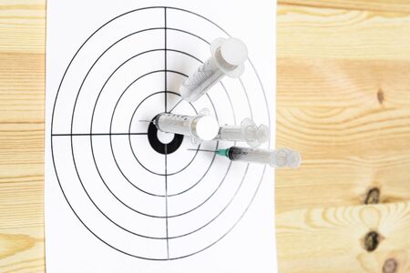 Four medical syringe hit the center of the rifle target. On the wooden background. Humor concept of therapy.の写真素材