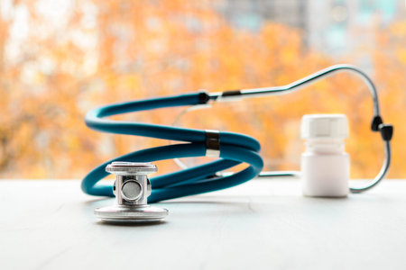 Stethoscope and white bottle with pills on white table, with autumn colors on background. Cold and the flu season treatment concept.の写真素材
