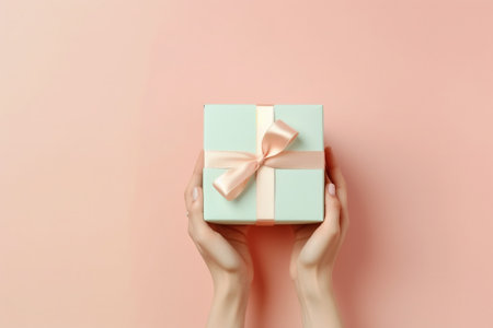 Female hands holding a gift box on a pink background. Flat lay, top viewの素材